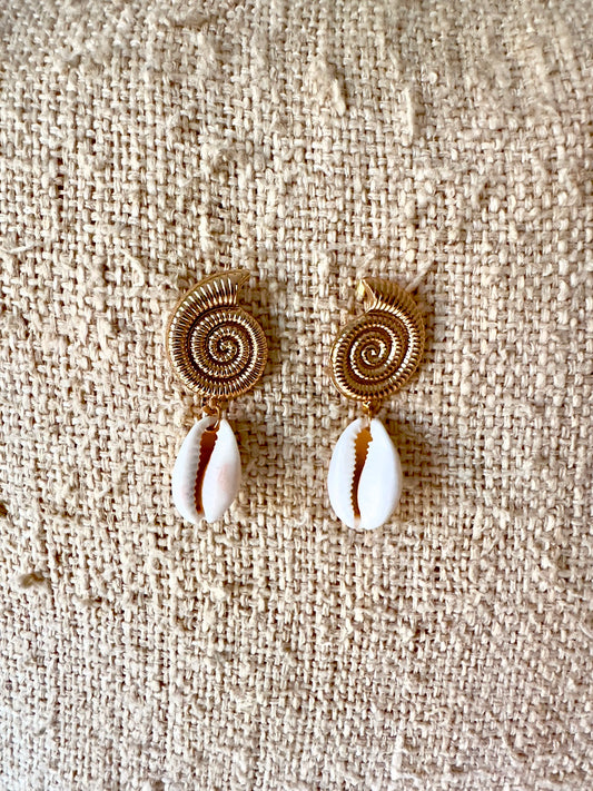 Pendientes Caracola Dorada sobre fondo de arpillera, vista cenital con espiral dorada y concha cowrie