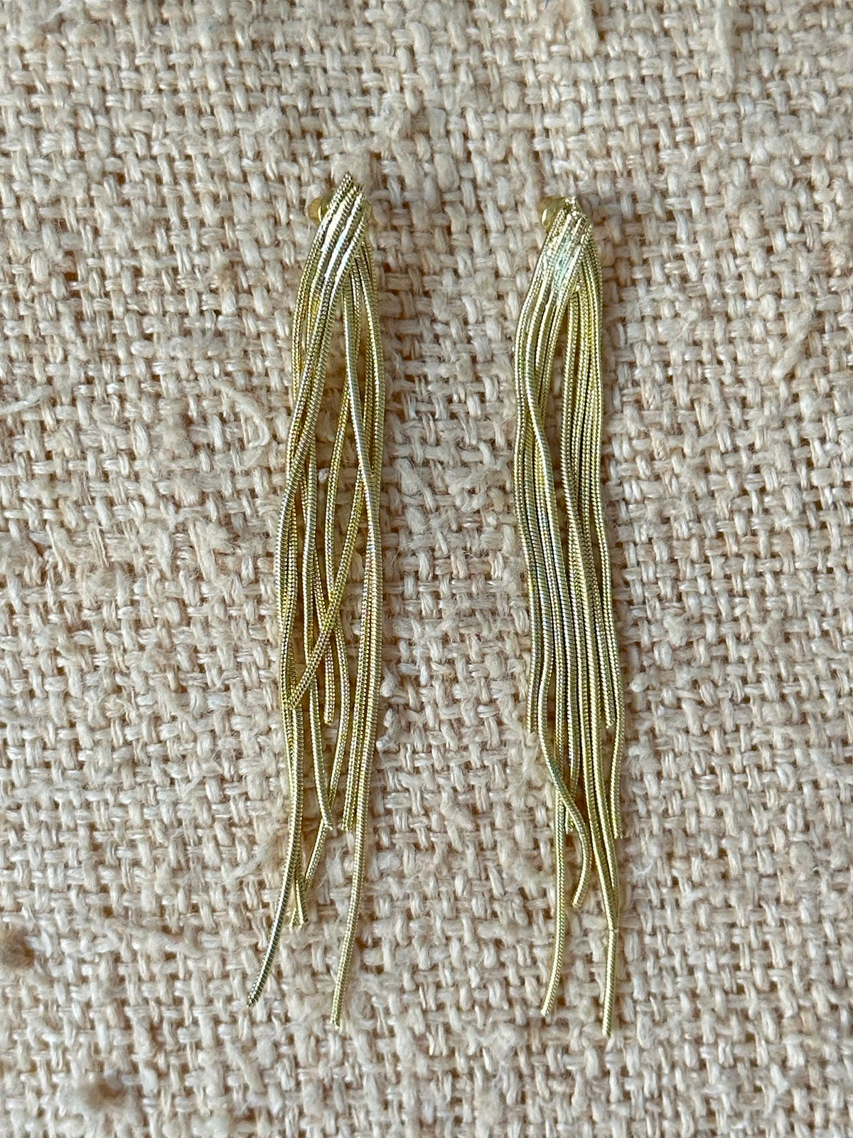 Pendientes flecos cadenas snake doradas sostenidos en mano, vista frontal